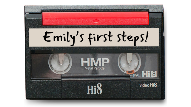 An 8mm tape with the label 'Emily's first steps!' written on it. Also called Hi8 video.