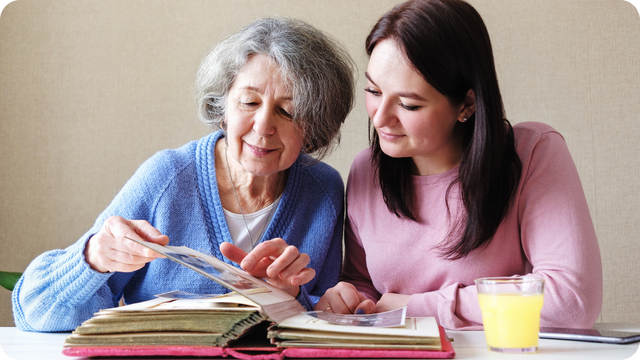 An adult child and aging parent sitting together at a table looking through old photo albums